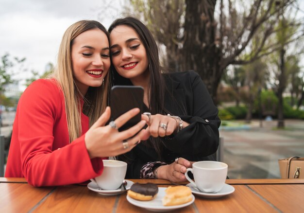 コーヒーショップに座って携帯電話を使用して2人の若い友人の肖像画。ライフスタイルと友情の概念。