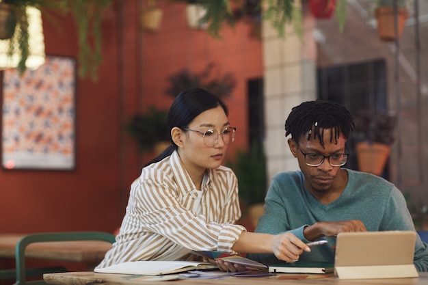 Portrait of two young people working on project together while sitting at table in cafe