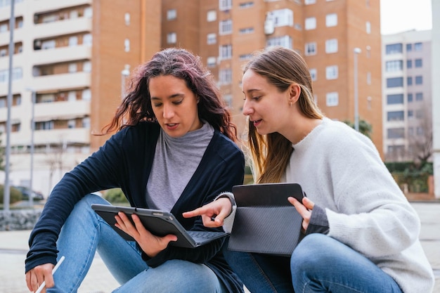 Portrait of two young woman students in university during break carrying laptop and books in hand