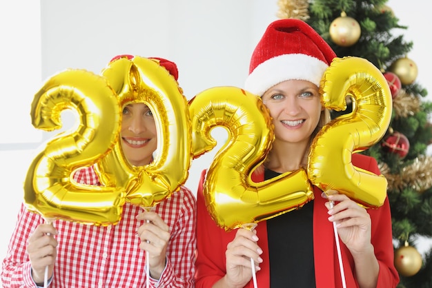 Portrait of two young women holding numbers in hands against of new year tree christmas