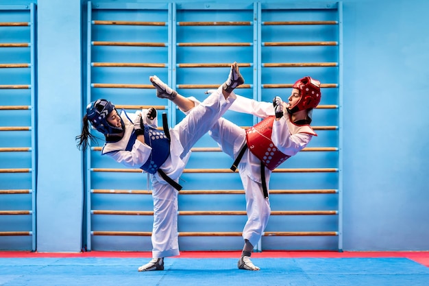 Photo portrait of two young women in kimono and suture taekwondo athletes wrestling in the gym sportswomen demonstrating taekwondo martial art hard training concept