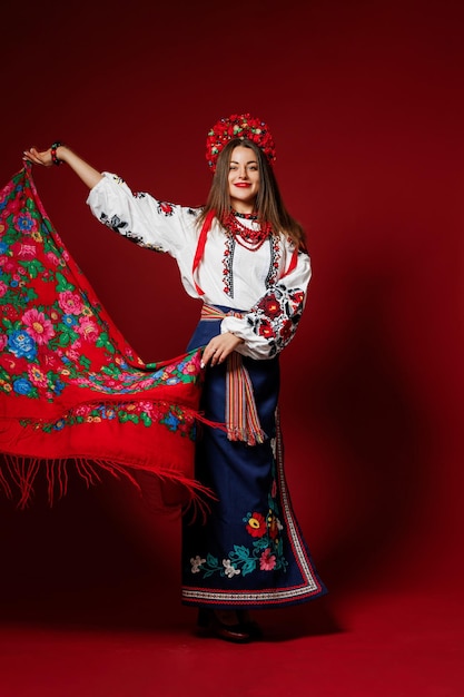 Portrait of ukrainian woman in traditional ethnic clothing and floral red wreath on viva magenta studio background twirls a handkerchief Ukrainian national embroidered dress call vyshyvanka