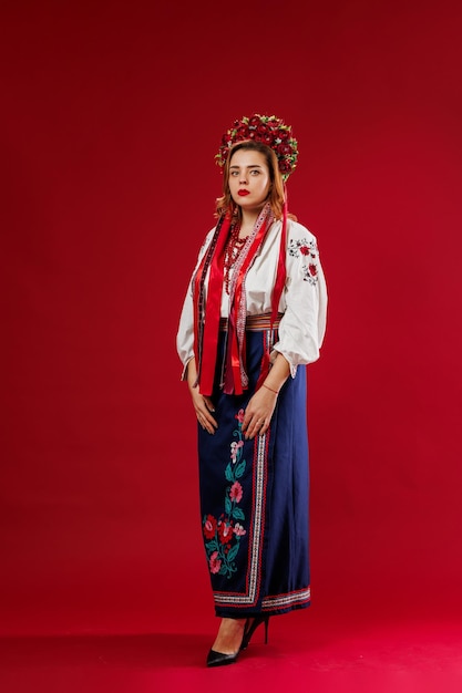 Photo portrait of ukrainian woman in traditional ethnic clothing and floral red wreath on viva magenta studio background ukrainian national embroidered dress call vyshyvanka pray for ukraine