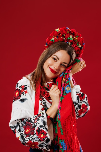 Portrait of ukrainian woman in traditional ethnic clothing and floral red wreath with handkerchief on viva magenta studio background Ukrainian national embroidered dress call vyshyvanka