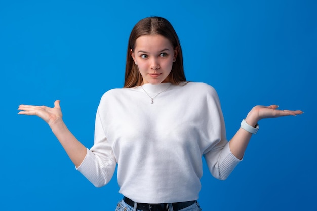 Portrait of uncertain young woman standing with raised arms on blue