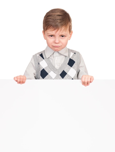 Portrait of a unhappy little boy with blank signboard isolated on white background Sad child holding banner and looking at camera Funny kid peeking from behind empty panel or placard board