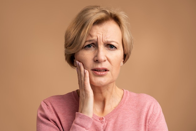 Portrait of unhealthy woman pressing sore cheek, suffering\
acute toothache, periodontal disease, cavities or jaw pain. indoor\
studio shot. dental problems concept