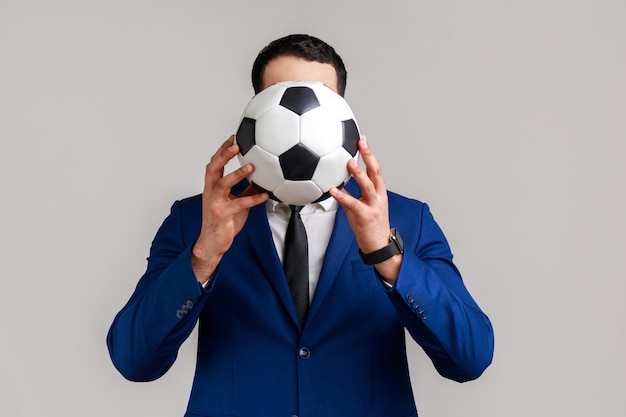 Портрет неизвестного анонимного бизнесмена, поддерживающего любимую команду, закрывающего лицо футбольным мячом
