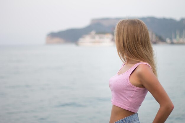 Portrait of unrecognizable young blonde woman looking at mountain by the sea horizontal