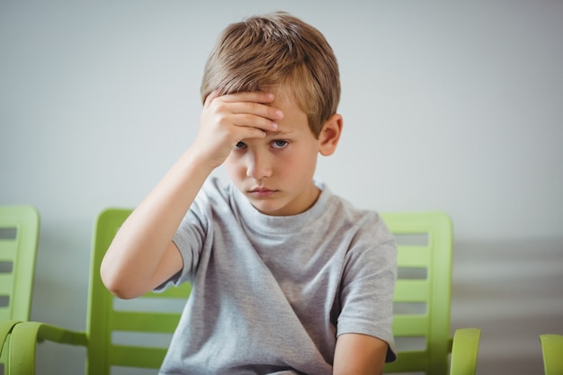 portrait of upset boy sitting on chair in corridor