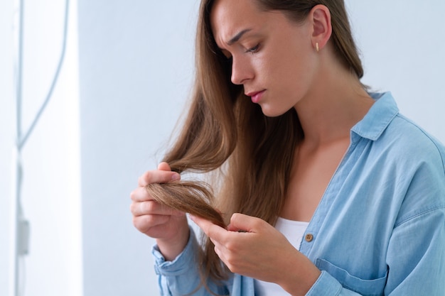 Portrait of upset unhappy sad woman with damaged lock of hair suffering from dry hair and split ends. 