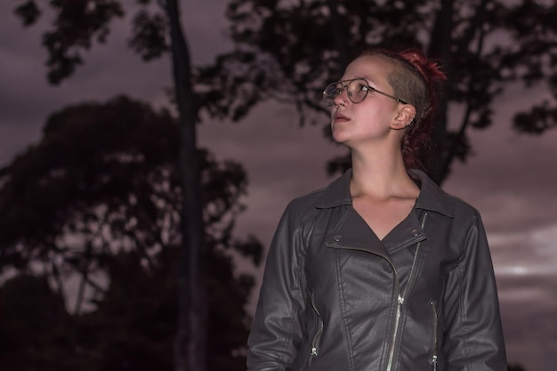 Portrait of an urban style young woman with a trendy haircut in glasses and retro leather jacket looking at right