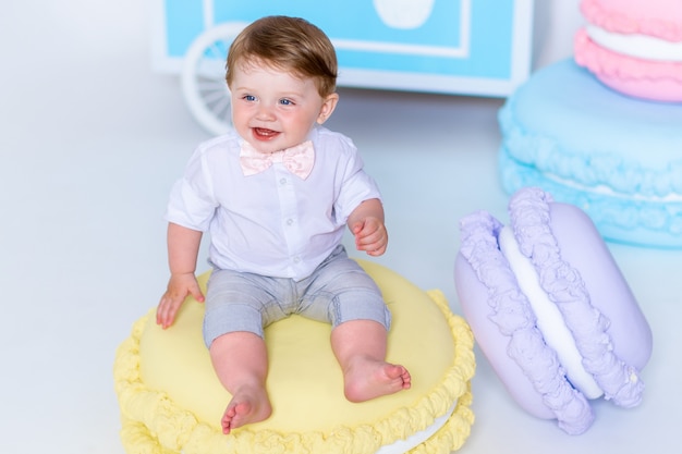 Portrait of very lovely little boy sitting on big macaroon and smiling.