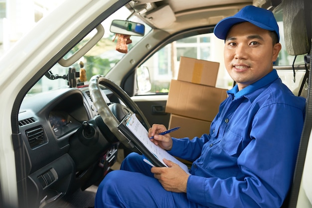 Portrait of Vietnamese develiry truck driver checking information in document before unloading vehicle