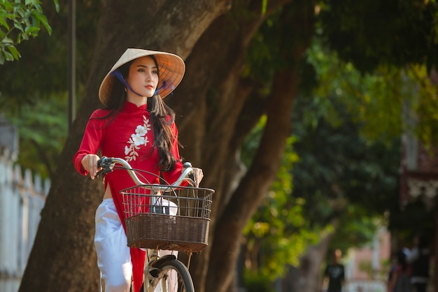 ベトナムの女の子の伝統的な赤いドレス、自転車でベトナムを着て美しい若いアジア女性の肖像画