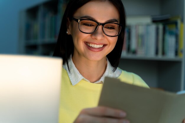 Portrait view of the happy smiling caucasian student woman\
reading book at library during the night education high school\
university learning and people concept