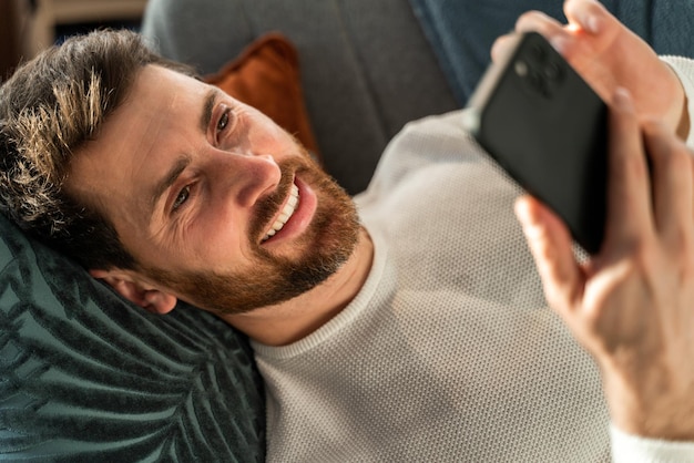 Portrait view of the young caucasian man messaging on smartphone at home with toothy smile. People and technologies concept