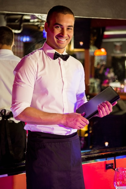 Portrait of waiter standing with a menu card in bar