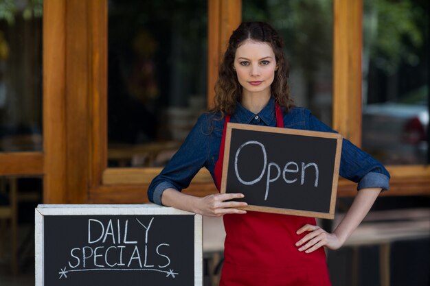 Portrait of waitress standing with chalkboard and menu