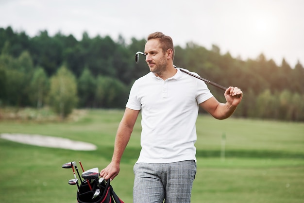 Photo portrait of walking golf player in the lawn and equipment in hands.