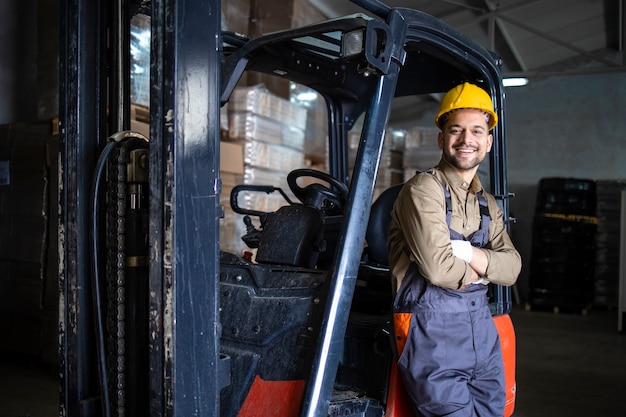 Portrait of warehouse forklift driver standing in storehouse by the machine.