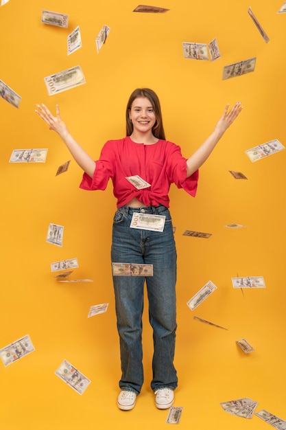 Portrait of wasteful rich woman with US dollars around on yellow background Vertical frame