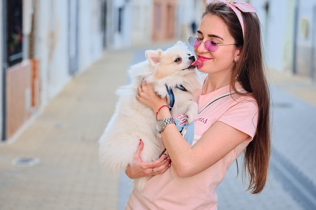 若い女の子の顔をなめる白いふわふわポメラニアン犬の肖像画。