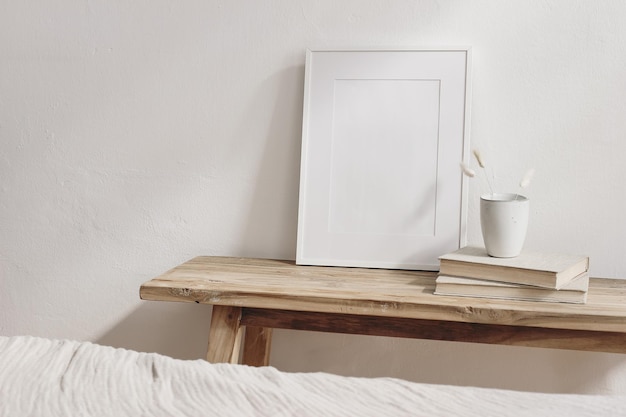 Portrait white frame mockup on vintage wooden console table Little ceramic vase with dry Lagurus ovatus grass on pile of books Blurred beige linen blanket in front Modern Scandinavian interior