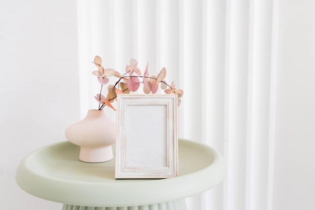 Portrait white picture frame mockup on table. Modern ceramic vase. Scandinavian interior.