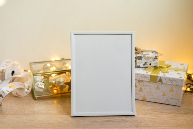 Portrait white picture frame mockup with christmas gifts, boken lights. High quality photo