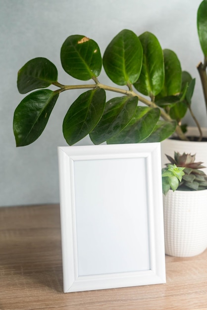 Portrait white picture frame mockup with white pots with succulents and zamiokulkas