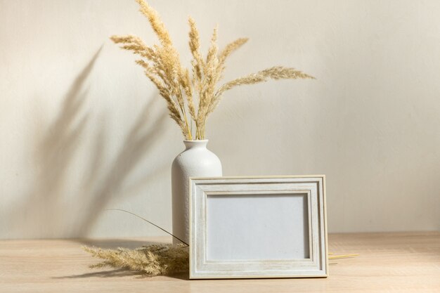 Portrait white picture frame mockup on wooden table Modern ceramic vase with dried flowers