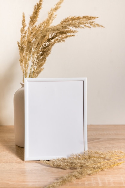 Portrait white picture frame mockup on wooden table Modern ceramic vase with dried flowers