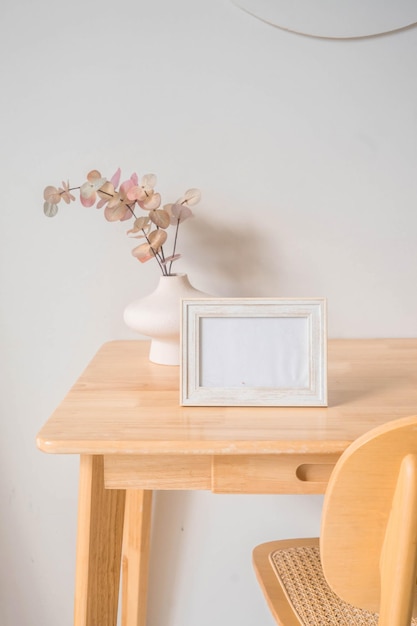 Portrait white picture frame mockup on wooden table. Modern ceramic vase with eucalyptus.