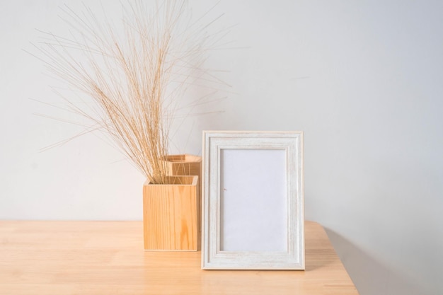 Portrait white picture frame mockup on wooden table. Modern ceramic vase with eucalyptus.