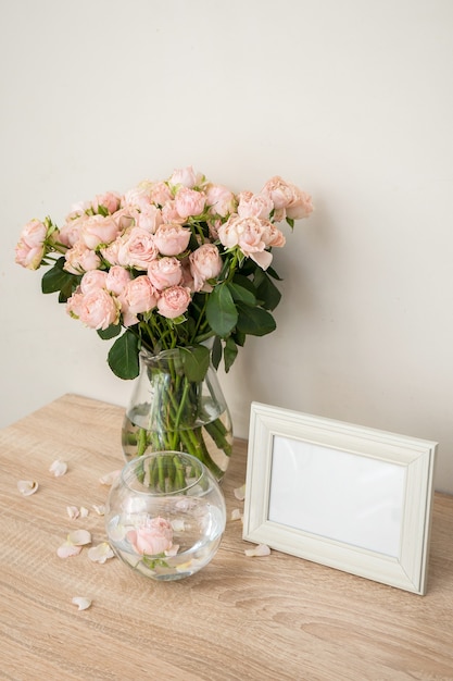 나무 테이블에 세로 흰색 액자 모형 장미와 현대 유리 꽃병 흰 벽 스칸디나비아 인테리어