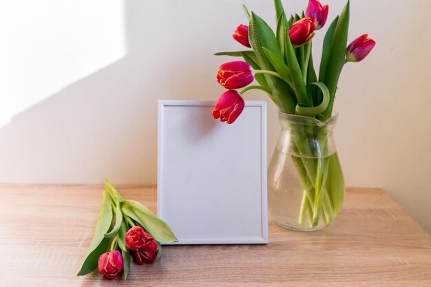 Portrait white picture frame mockup on wooden table Modern vase with tulipsScandinavian interior