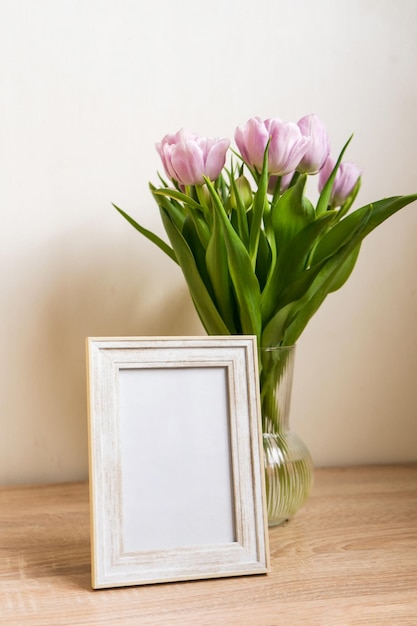 Portrait white picture frame mockup on wooden table Modern vase with tulipsScandinavian interior