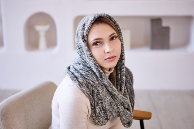 Photo portrait of white woman in headscarf who sits on couch in lounge