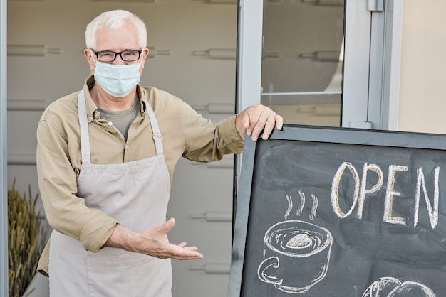 Portrait of whitehaired mature owner of store or cafe pointing at open signboard