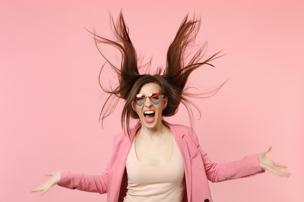 Foto ritratto di giovane donna urlante selvaggia in occhiali a cuore che salta con capelli fluenti isolati su sfondo rosa pastello in studio. persone sincere emozioni, concetto di stile di vita. mock up spazio di copia.