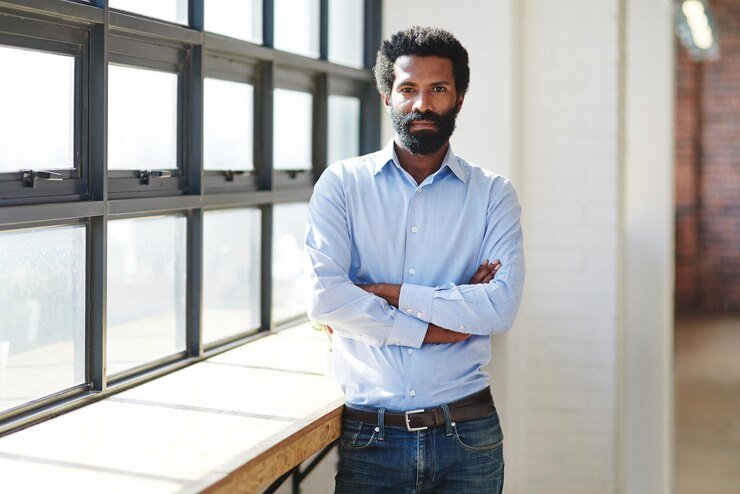 Photo portrait window and a business man arms crossed in the office with a mindset of focus on future success serious vision and corporate with a male employee standing in the workplace during his break