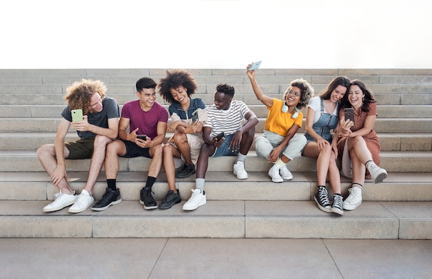 Portrait with copy space of group of mixed race people with smart phones excited students using thei...