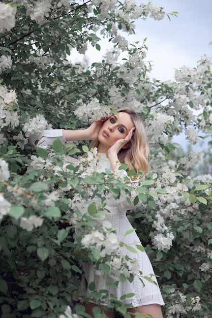 Portrait of a woman in an Apple orchard in a white dress.