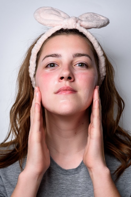 Portrait of woman applying cream on a clean fresh face on gray