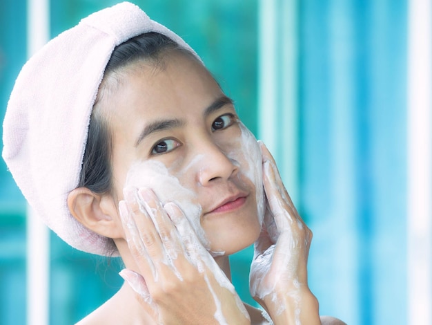 portrait of woman applying soap on cheek in bathroom