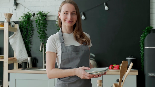 Портрет женщины в фартуке стоит с тарелками в руках на кухне