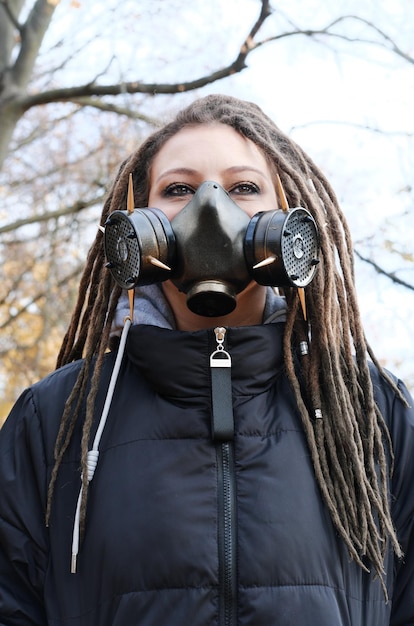 Photo portrait of a woman in a black jacket with dreadlocks and a gas mask with spikes