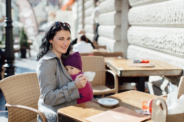 Photo portrait of woman carrying son in scarf on chair at sidewalk cafe