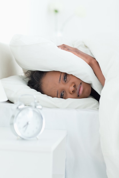 Portrait of a woman covering her ears while her alarm clock is ringing